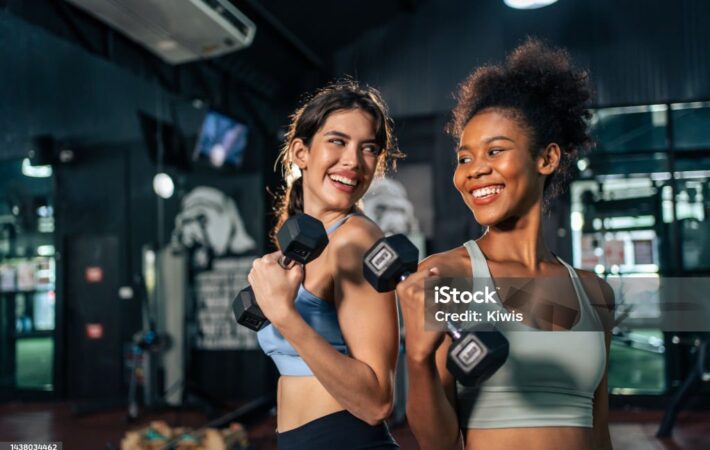 Latino and African sport woman exercising and build muscle in stadium. Active strong beautiful fit athlete girls in sportswear workout lifting weight dumbbell for arm and health care at fitness club.